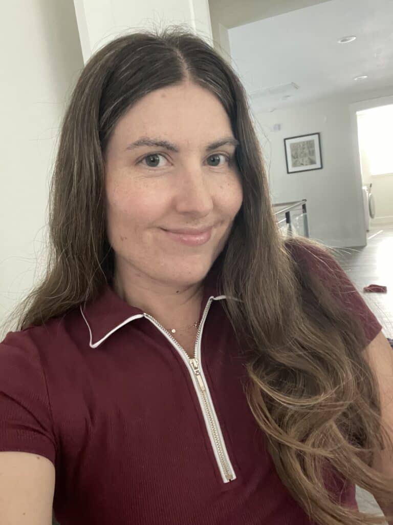 Woman with long brown hair taking a close-up selfie indoors, wearing a burgundy zip-up top